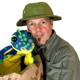 Diggery Digger in green jungle gear holding his blue and yellow with green spots dinosaur puppet. Family show.